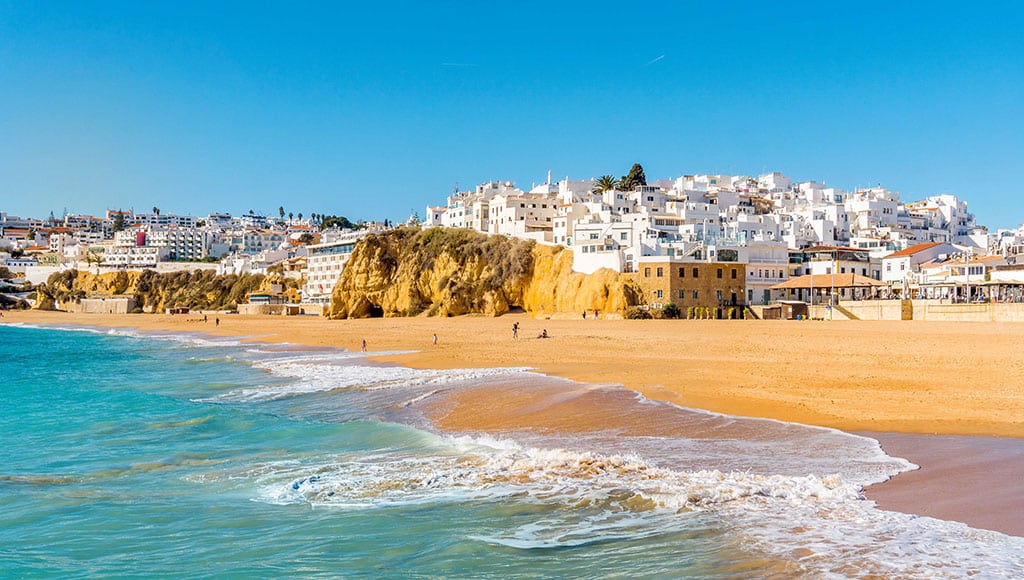 Wide sandy beach in white city of Albufeira, Algarve, Portugal|Hourglass on the background of the Portugal flag, the concept of time and countries, space for text