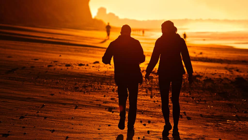 Two people walking down the Algarve beach in Portugal during early morning backlit by the sun.