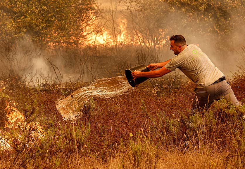 A local throwing a bucket of water onto the burning brush – Photo: LUÍS FORRA/LUSA|Odemira fire: flames raging close to Aljezur on Monday, August 7 – Photo: LUÍS FORRA/LUSA