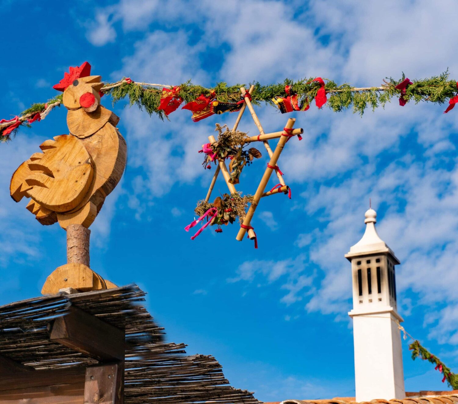 A rooster crows at the Christmas star_|Cooking workshop at Parises Natal - Photo: Nunes Mata|A cat with Serra de São Bras beyond|Antique hats are festive decorations|Antiques of village life||Visitors of Parises enjoy a dancing event - Photo: Filipe Nunes Mata|Parises is a star village|Cart of hearts|Real bread|Sonia Martins, Isabel Rodrigues, Celeste Conceisão of Parises|The wonderland of Parises|Wise owl decoration