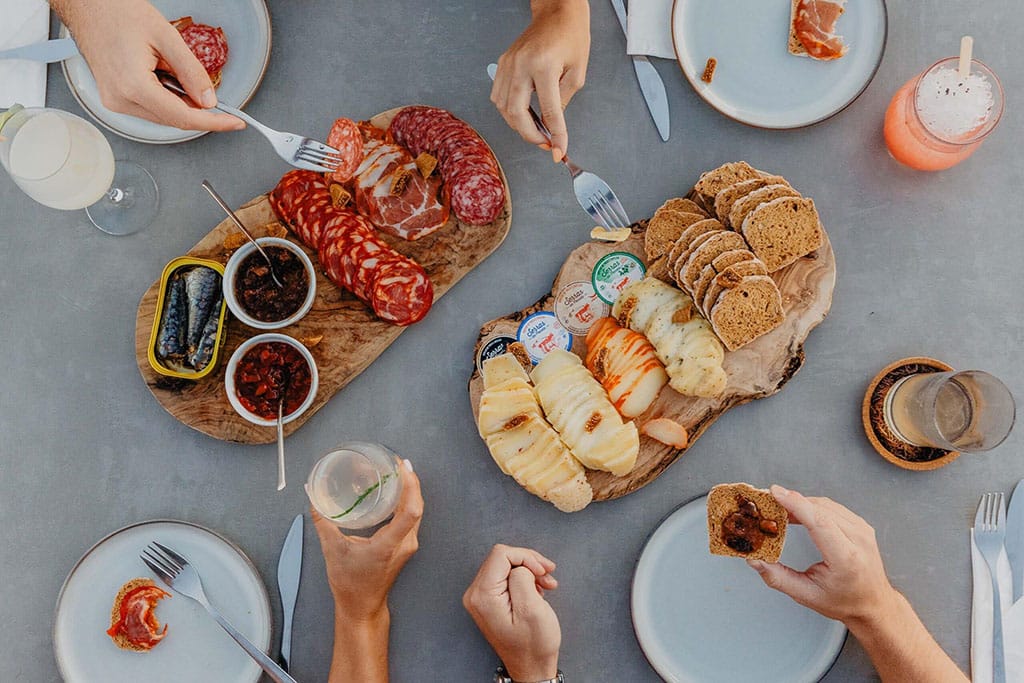 Photo of table with various tapas|two couples enjoying drinks by the becah