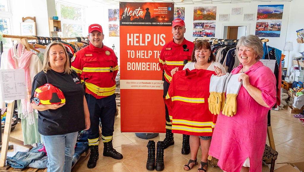 Alerta volunteer Karina Bettis, Bombeiros Cristiano Quaresma, Luís Correia, Alerta founder and shop manager Debby Burton, and volunteer Karen Evans|Alerta Charity Shop|Clothing and books at Alerta Charity Shop|Cookbook display at Alerta Charity Shop|Debby Burton chats with a customer at Alerta Charity Shop