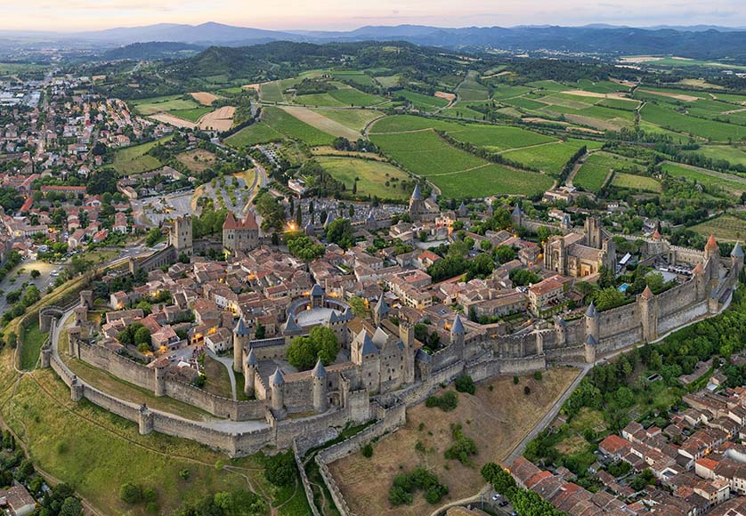 Aerial view of the Carcassone citadel|The façade today, as it was painted by Monet 130 years ago|The west façade of Rouen’s Notre Dame Cathedral, clearly showing the tower of Saint Romain (on the left) and the Butter Tower (on the right)|The cathedral’s semi-cloister in the Cour D’Albene|The rue du Gros-Horloge, with its attractive 15C-17C half-timbered houses and the clock itself, one of Rouen’s most popular monuments|Helga enjoying oysters and a cold white wine in the Place du Vieux-Marché|St George rampant on top of the Cathedral|The Cathedral St-Étienne, seen from a vantage point on the heights behind the Lot river|The Pont Valentré, a fortified pedestrian bridge built in the 14th century.|The barbican of the Pont Valentré|A side view of the Cathedral, showing the heavily fortified façade and the two cupolas|The cloisters of the cathedral|The town of Puy-l’Évêque near Cahors in the heart of the wine region|The main gate of the Carcassonne citadel|The outer ramparts of Carcassonne|The entrance to the Château Comtal, showing the moat and entry bridge