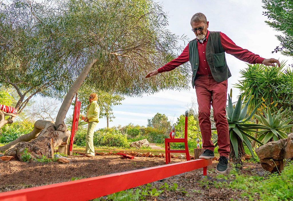 Gerhard approaches the balance beam|A-fun-way-to-exercise-scaled|Gudrun-is-on-the-stilts-and-Gerhard-on-the-rocker-scaled|Swinging bridge reqires good balance|Tree-stumps-and-a-swinging-platform-provide-balance-training-scaled