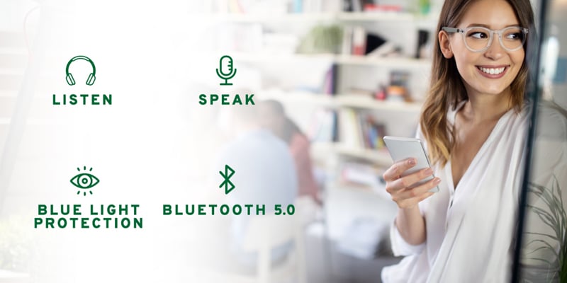 An optician holding a pair of smart glasses and showing all its features namely Bluetooth 5.0, ability to listen and speak through them, and blue light protection