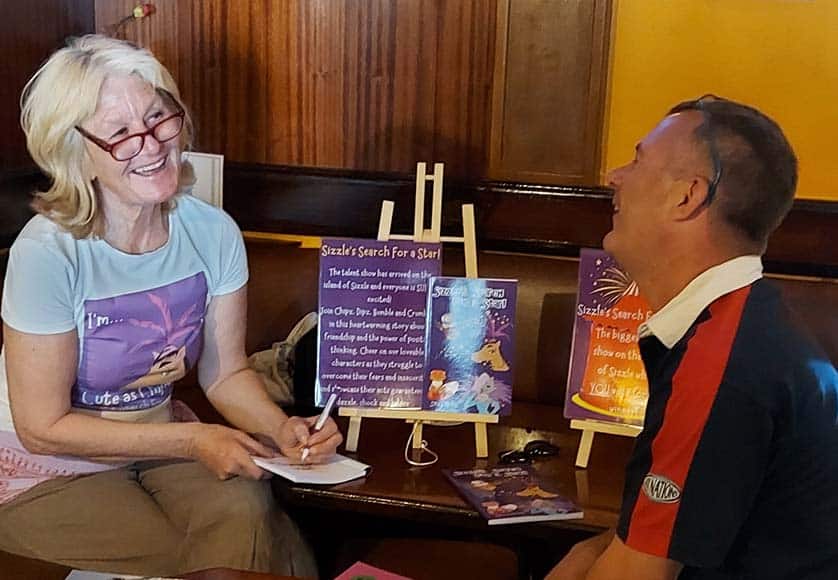 Sally Green signing one of her books|P. D. Cain displaying some of his published books|Peter & Sally showing their books
