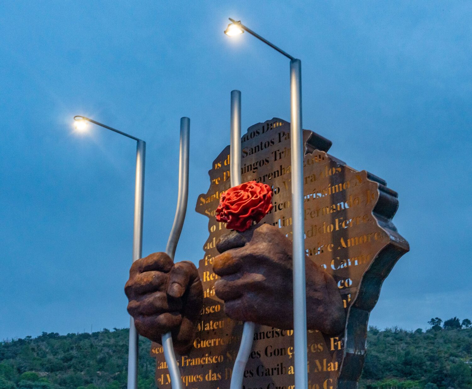 The lit scupture stands proudly against the dusky sky|Silves dignitaries and residents pose with the artistic creators|Silves residents reading the names on the plaque|Rosa Cristina Gonçalves da Palma, President of the Silves Cámara, admires the sculpture|Producer Pedro Bartiloti, sculptor João Franck, and metalworker Bruno Franca|Former political prisoner Gregorio Miguel Patricio (91) poses with his daughter Fatima and granddaughter Vera