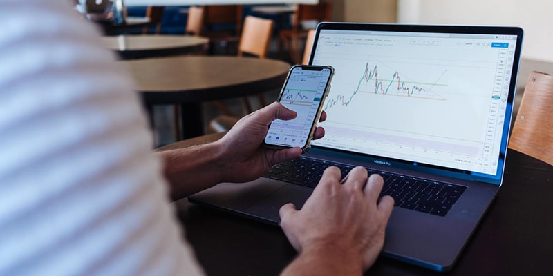 Man looking at laptop and mobile with forex app open