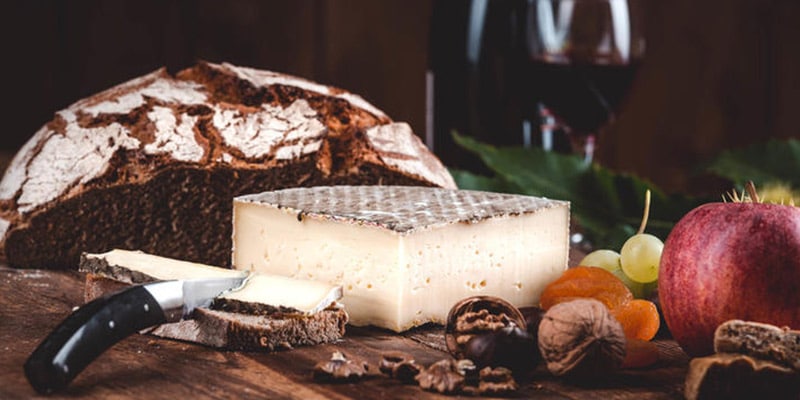 Photo with cheese, bread, some nuts and a glass and bottle of wine on the background|Photo of a large french cheese
