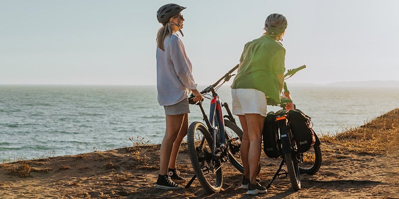 Two women by their e-bike enjoying the Atlantic Coast Route views|Tow women riding their e-bikes through the Atlantic Coast Route in the Algarve|