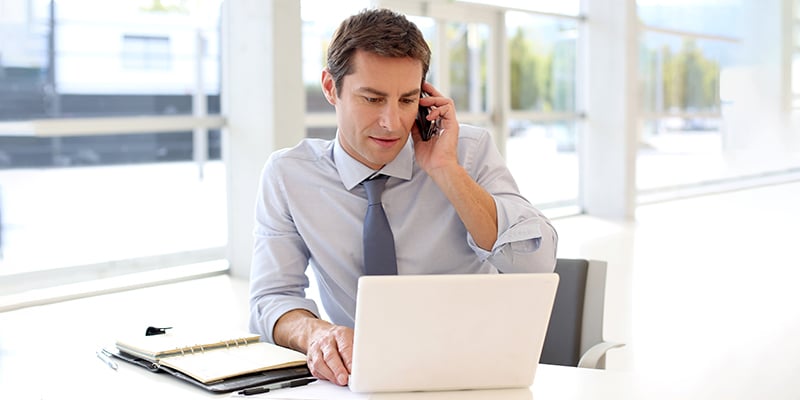 Man answering cell phone in front of a laptop