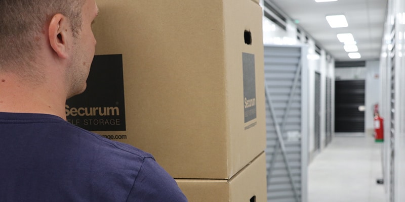 Partial image of a man carrying card boxes in a corridor at Securum Self Storage|Aerial view of the Securum Self Storage facilities near Loulé