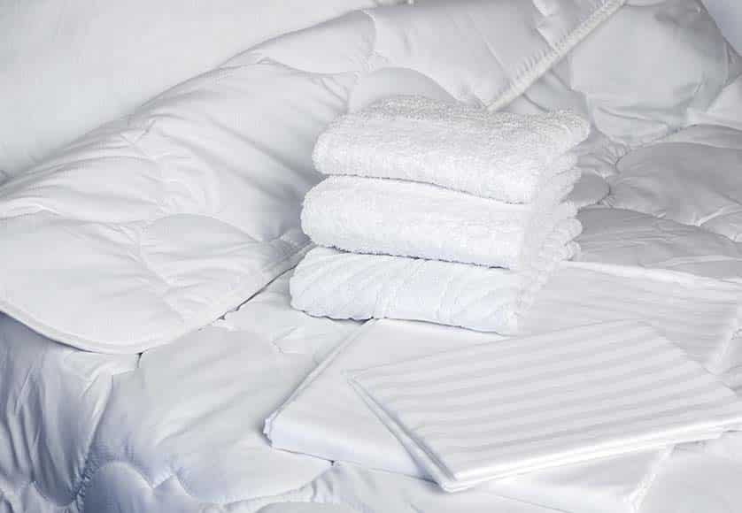 Towels are on bed. White bedding close-up. Clean terry towels on bedstead. Concept - bed linen at hotel. Sewing industry. Several towels lie on in a pile. Sale of sets with bed linen. Textile