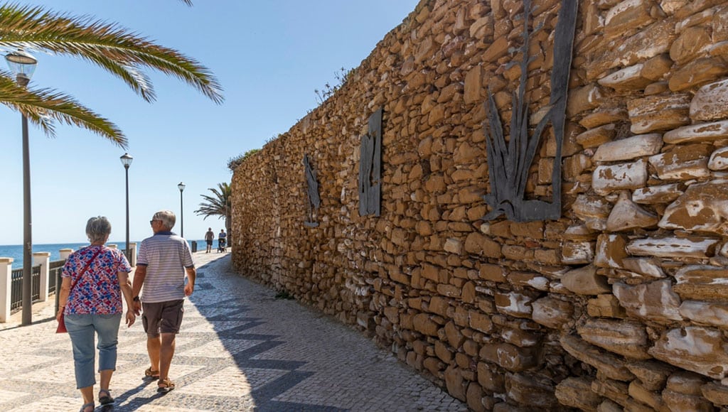 Elder couple walking in Luz beach near Lagos in the Algarve region, Portugal.|Retirement, fitness and walking with dog and couple in neighborhood park for relax, health and sports workout. Love, wellness and pet with old man and senior woman in outdoor morning walk together|Time for Taxes Money Financial Accounting Taxation Concept