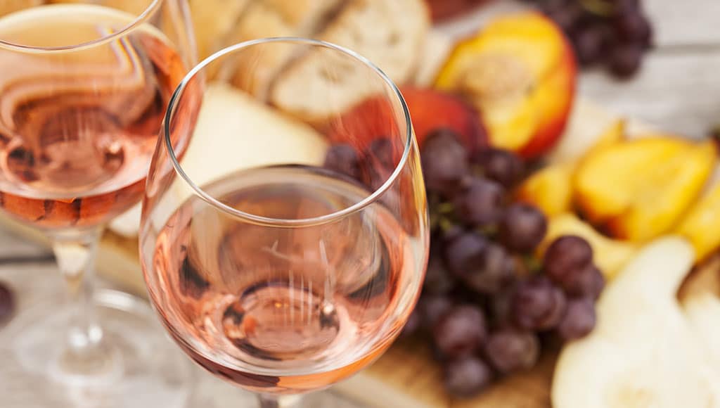 Two glasses of rose wine and board with fruits, bread and cheese on wooden table, shallow DOF|Negra Mole|WINE