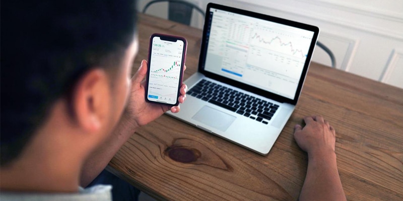 Man looking at smartphone app and laptop screen with trading platforms open