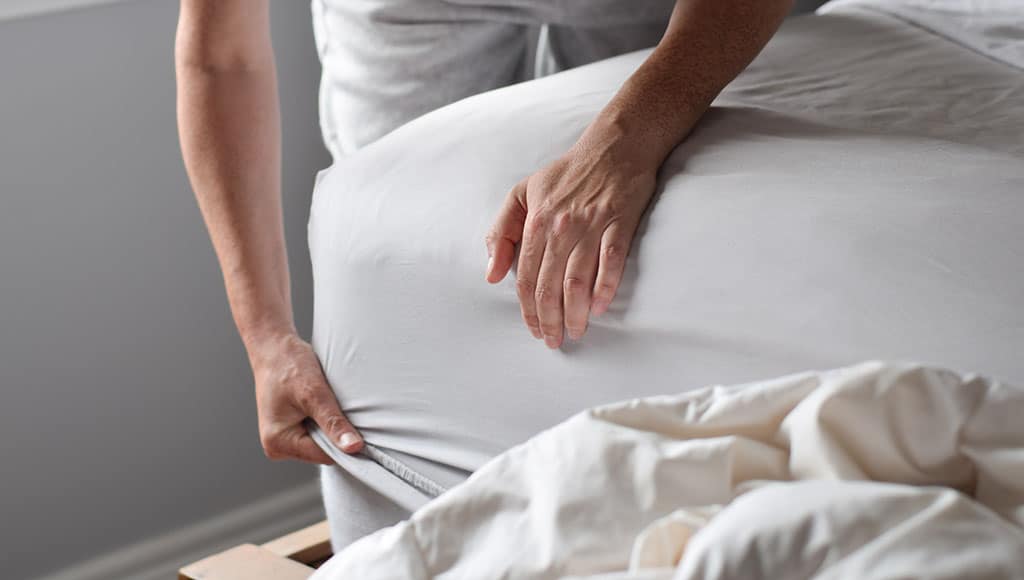 Woman is putting on a fitted sheet on a mattress while making the bed