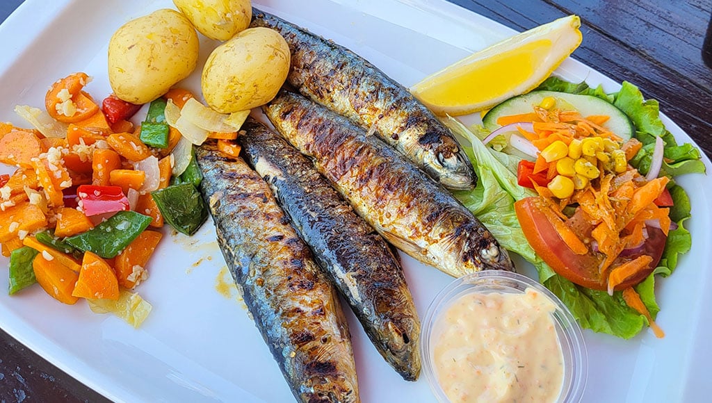 Sardines by the coast - Simple, smoky, perfectly Portuguese: grilled sardines with salad on a sunlit seaside table.